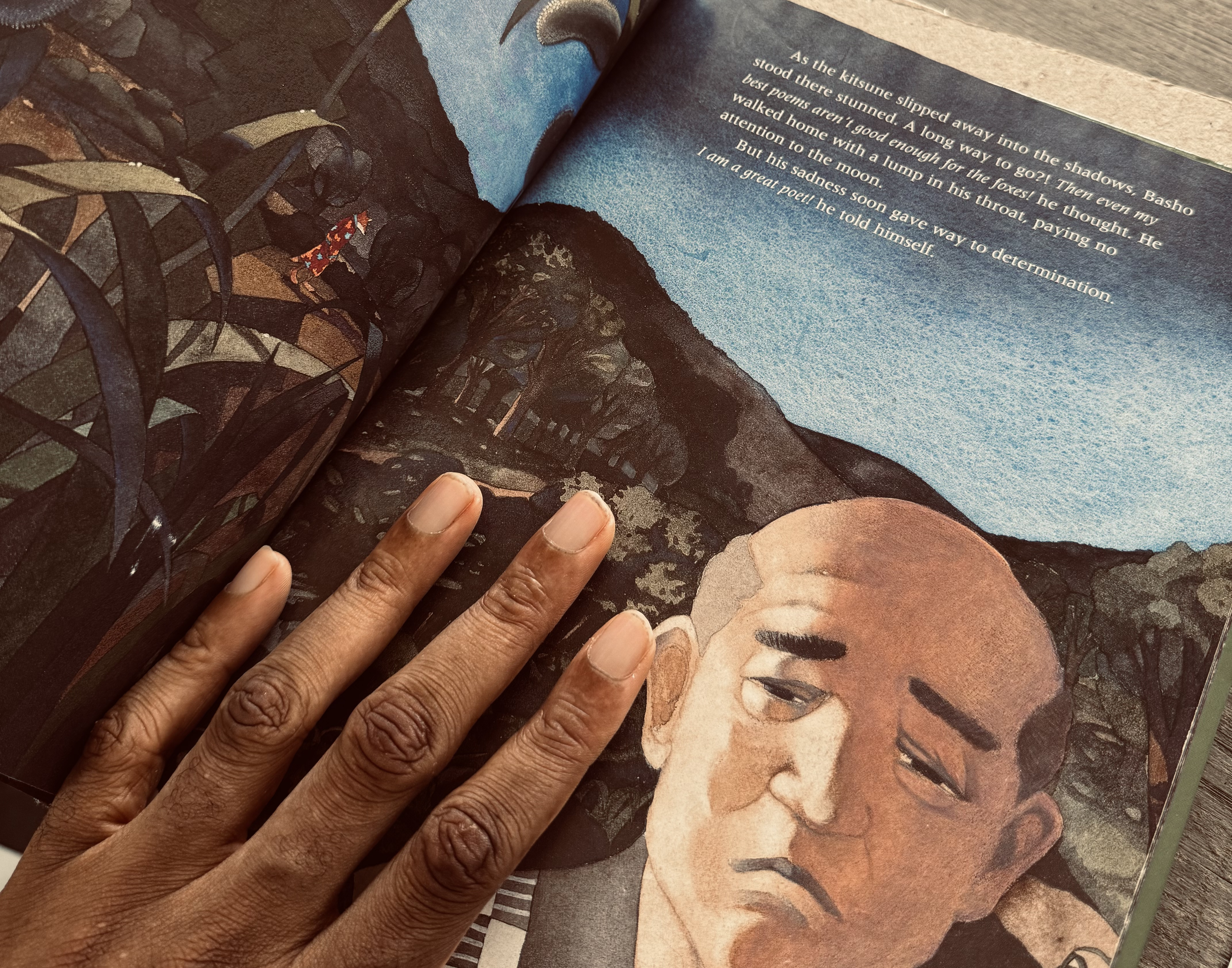 A hand resting on an illustrated page from Basho and the Fox - a story about becoming a poet by first learning to be honest.